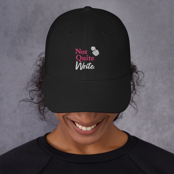 A model wears a black baseball cap featuring an embroidered Not Quite Write logo with two balls of scrunched paper.