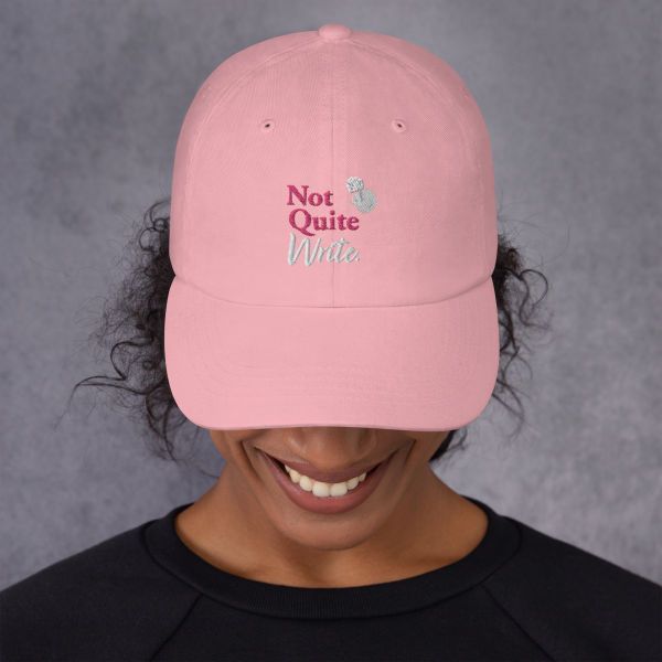 A model wears a pink baseball cap featuring an embroidered Not Quite Write logo with two balls of scrunched paper.